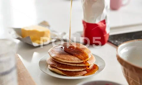 Maple Syrup Being Poured On Stack Of Freshly Made Pancakes Or Crepes On Table Stock Photos