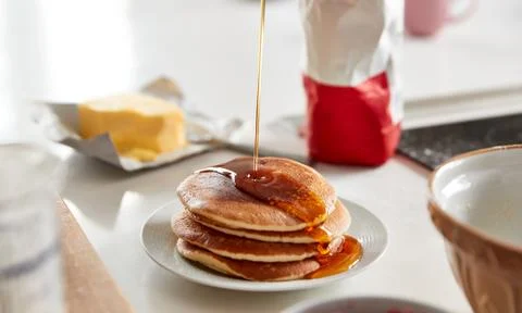 Maple Syrup Being Poured On Stack Of Freshly Made Pancakes Or Crepes On Table Stock Photos