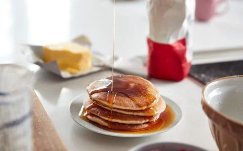 Maple Syrup Being Poured On Stack Of Freshly Made Pancakes Or Crepes On Table Foto stock
