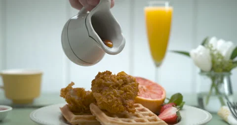 Maple syrup is poured over a plate of fried chicken, waffles and fruit with a cu Stock Footage 199459323