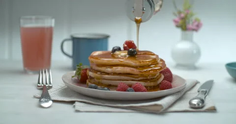 Maple syrup is poured over a stack of pancakes with fruit and butter on a table Stock Footage 199462998