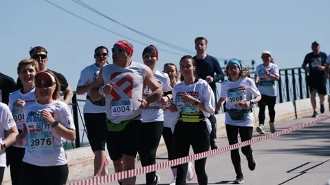 Marathon runners wearing numbered bibs crossing bridge finish line, showcasing Stock Footage 310059641