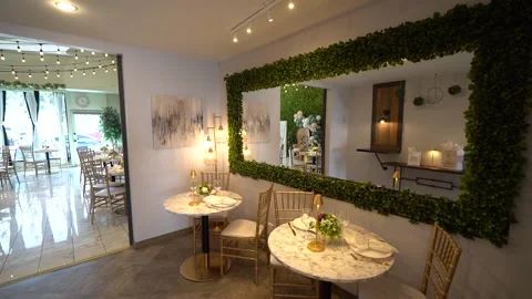 Marble bistro tables beside a large greenery-framed mirror Stock Footage 345553475