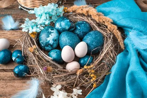 Marble-blue Easter eggs in a wicker nest with feathers and flowers next to a Stock Photos
