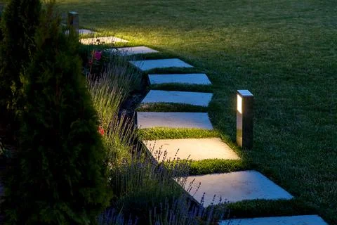 Marble path of square tiles illuminated by a lantern glowing with warm light. Stock Photos
