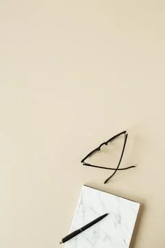 Marble styled notebook, pen, glasses on pastel beige background. Minimalist h Stock Photos