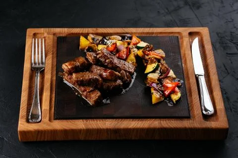 Marbled beef steak with vegetables and sauce on a black backgrou Stock Photos