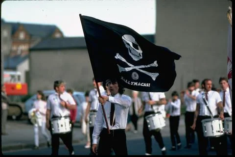 Marchers w. skull & crossbone flag w. out-of-focus drum corps behind in Orange P Stock Photos
