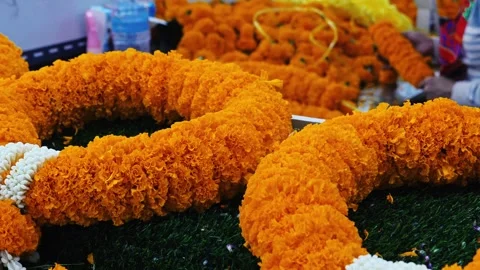 Marigold flower garlands resting on grass with worker in background Stock Footage 335073761