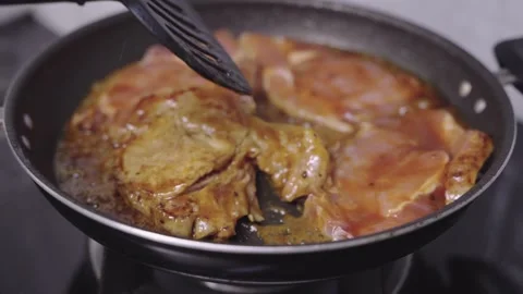 Marinated pork steaks sizzling in a black non-stick skillet on a stovetop. .. Stock Footage 339513154