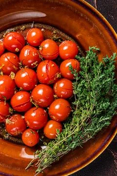 Marinated Preserve cherry tomatoes in a rustic plate with garlic and thyme. Dark Stock Photos