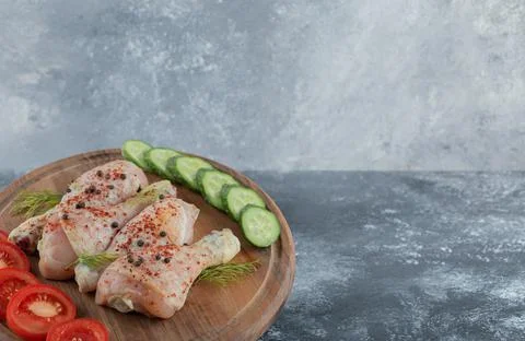 Marinated raw chicken drumstick with vegetable on wooden board Stock Photos