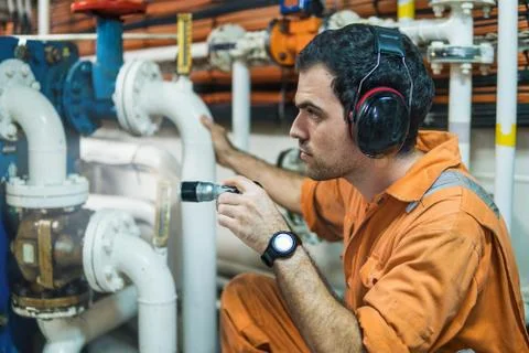 Marine engineer inspecting ship's engine in engine control room Stock Photos