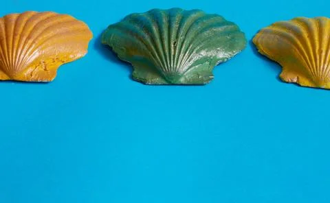Marine layout. Three seashells painted orange, yellow, and green on a blue ba Stock Photos