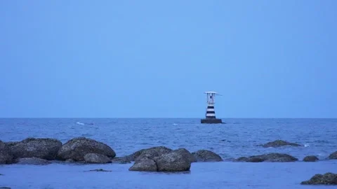 Maritime lighthouse with red blinking light against serene blue horizon in Stock Footage 314973913