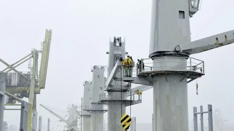 Maritime Workers Inspecting Heavy Cargo Ship Cranes During Rainstorm at Port Stock Footage 331165970