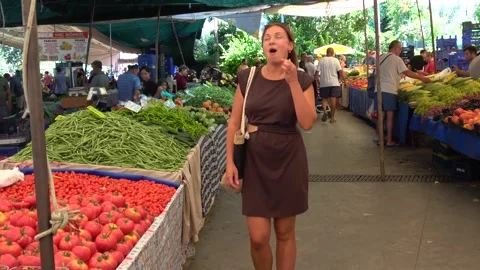 At the market a woman eats a fresh cherry tomato with a joyful expression of Stock Footage 343557510
