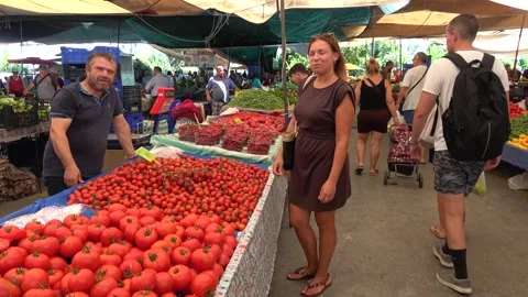 At the market a woman eats a fresh cherry tomato with a joyful expression of 스톡 동영상 343557563