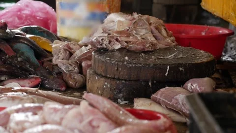 A market worker cuts fish into pieces on a round wooden block near products and Stock Footage 338001464