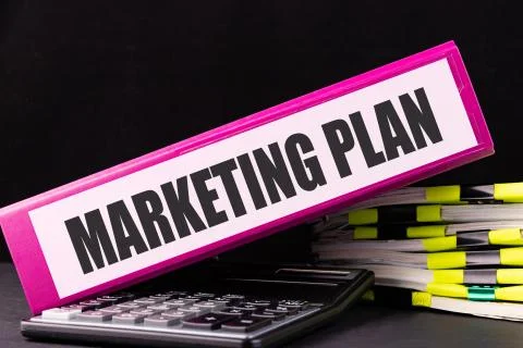 MARKETING PLAN text is written on a folder lying on a stack of papers on an o Stock Photos