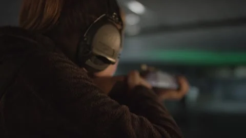 Marksman in Ear Protection Aiming Down Indoor Range, Green Light, Rear View Vídeo Stock 341318516