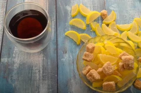 Marmalade lemon slices, pieces of brown sugar and a glass of black tea on a w Stock Photos
