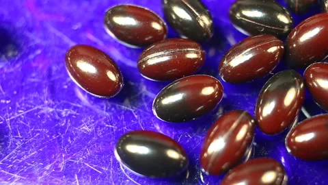 Maroon and black oval spindle-shaped capsules in a shiny gel shell move smoothly Stock Footage 144855238