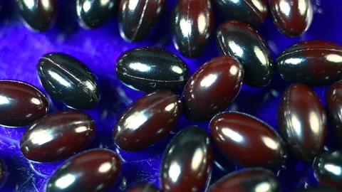 Maroon and black oval spindle-shaped capsules in a gel shiny shell extremely clo Stock Footage 144855308