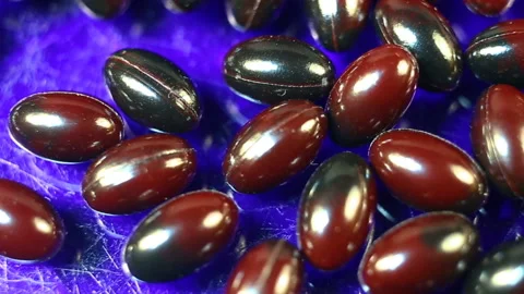 Maroon and black oval spindle-shaped capsules in a shiny gel shell move smoothly Stock Footage 144855342