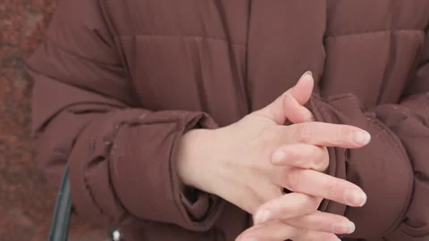 Maroon quilted puffer jacket with hands rubbing together for warmth, showing Stock Footage 345659172