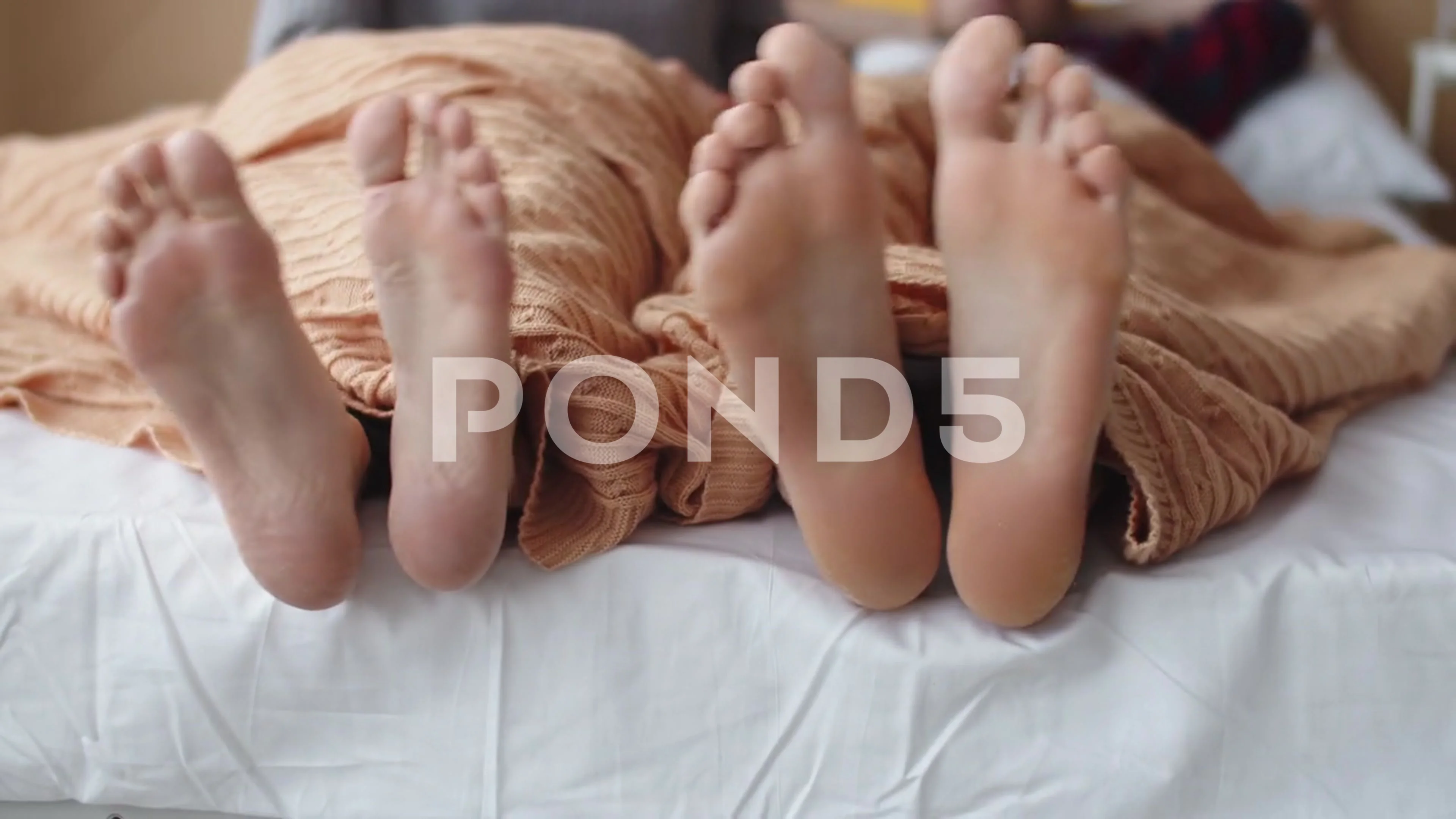 Married couple feet are moving under blanket in bed in funny rhythm, couple is
