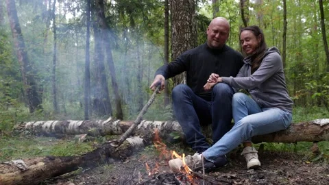 A married couple on a hike through the forest stopped to warm up by the fire sit Видео 159640192