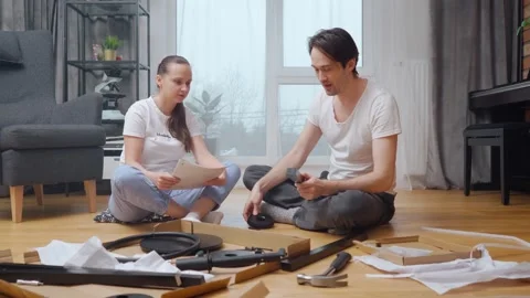 A married couple independently assembles new furniture from a set of parts. Stock Footage 261187740