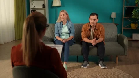 A married couple sits on a couch in front of a marriage counselor. The expert on Stock Footage 252399774
