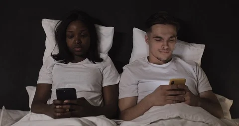 Married multi-ethnic couple lying in bed at night and using smartphones. Woman Stock Footage 112085543