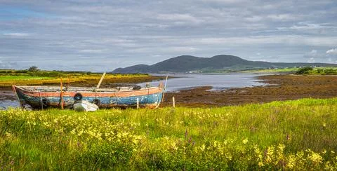 Marsh after ebb tide with old rusty paddle boat and mountain range in the bac Stock Photos