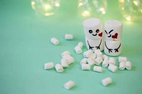 Marshmallow men on a mint turquoise background illuminated by a garland Stock Photos
