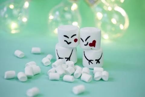 Marshmallow men on a mint turquoise background illuminated by a garland Stock Photos