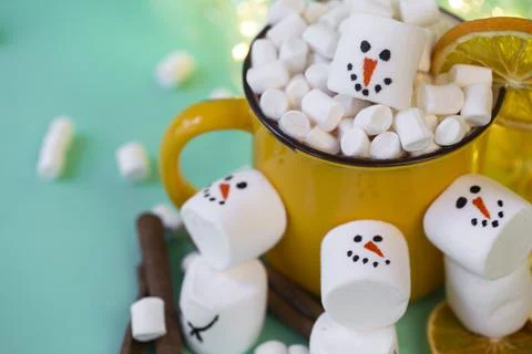 Marshmallow snowmen on a mint turquoise background with a yellow cocoa mug il Stock Photos