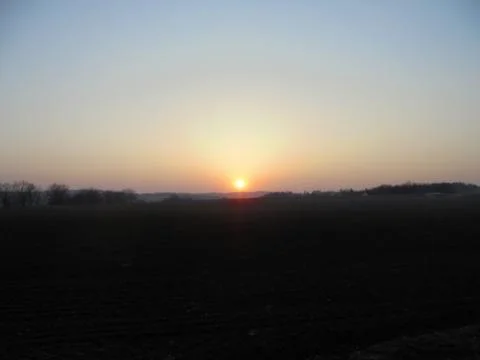 Marvelous sunset over dark fields under bright sky. Stock Photos