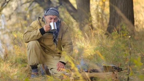 Masculine hunter drinks tea by the fire Stock Footage 84149606
