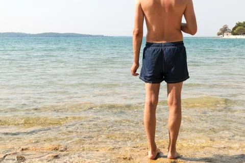 Masculine model of backs looking at the sea. Clear water, bright sun and Stock Photos