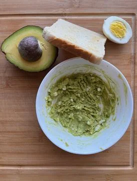 Mashed avocado with boiled egg and bread on a wooden cutting board. Stock Photos