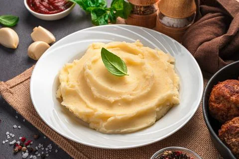 Mashed potatoes in a white plate with basil close-up. Stock Photos