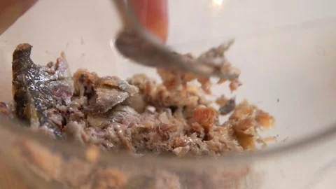 Mashing canned sardines using fork in glass bowl on white table closeup Stock Footage 121364413
