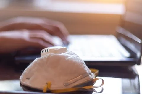 Mask on the table, while a person uses a laptop to work from home Stock Photos