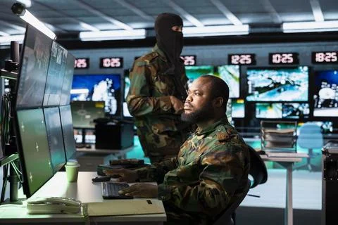 Masked armed soldier guarding computer operator in war room Stock Photos