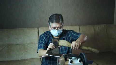Masked asian man sharpens axe on a grinder. Work process Stock Footage 143673434