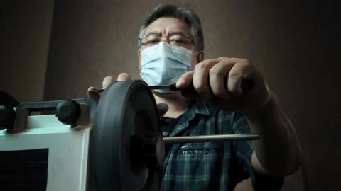 Masked asian man sharpens knives on a grinder Stock Footage 143673014