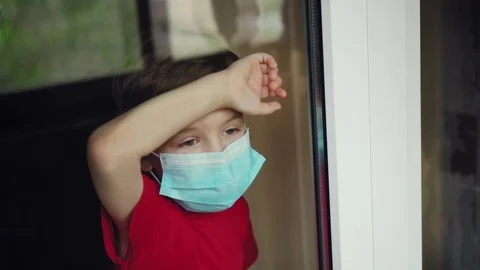 A masked boy looks out the window Stock Footage 129338562